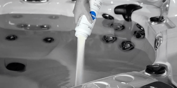 Person pours a liquid from a bottle into a hot tub with visible jets in the background.