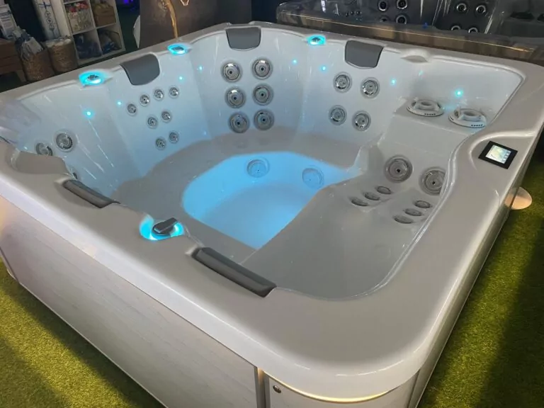 White rectangular hot tub with numerous built-in massage jets and blue LED lighting, shown on a showroom floor.