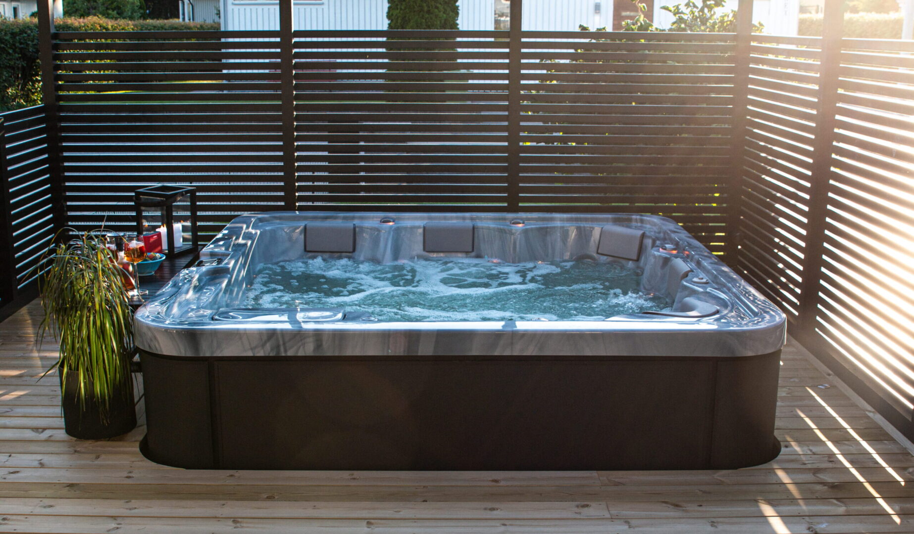 Outdoor hot tub on a wooden deck, bordered by horizontal slat privacy fencing; bubbling water in the tub.